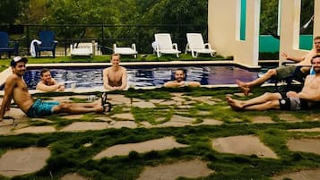 Eine Gruppe von Männern sitzt am Pool, im Hintergrund ein gepflasterter Weg und viel Grün.