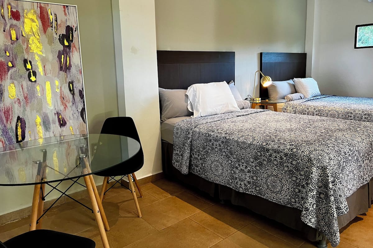 Habitación de hotel con dos camas, una mesita de cristal y un cuadro abstracto moderno.