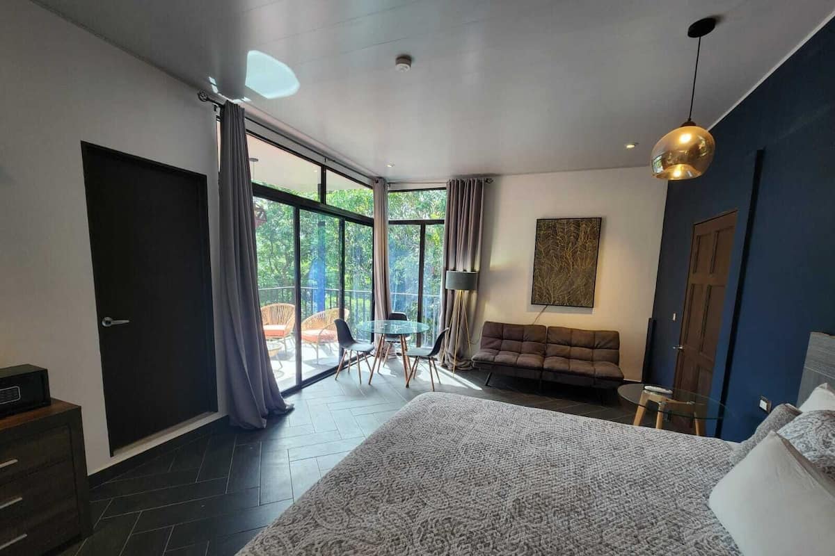 Un dormitorio moderno con una cama grande, un sofá, una mesa de comedor y un balcón con mobiliario exterior.