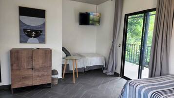 Un dormitorio moderno con cama, escritorio, televisor y balcón con cortinas.