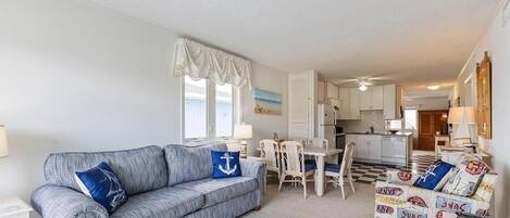 Una sala de estar con sofá, una mesa de comedor y sillas. Se observa una zona de cocina al fondo.