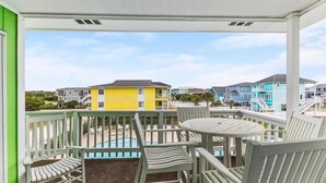 Un balcón con vistas a casas coloridas, una piscina y una mesa con sillas.