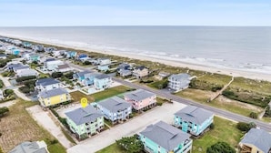 Vista aérea de una zona residencial costera con casas a lo largo de la playa, una carretera y una vista despejada del océano.