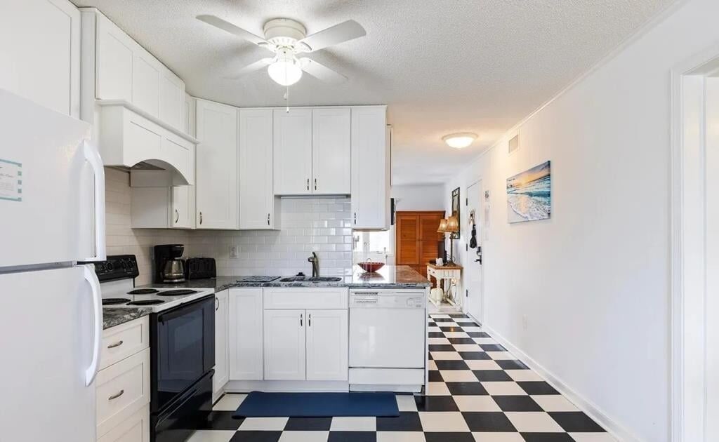 A kitchen with white cabinets, a black and white checkered floor, a ceiling fan, and a black stove.