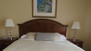 A neatly made bed with a white bedspread and striped pillows, a wooden headboard, two bedside lamps, and a framed painting above the bed. - Laguna Lodge (Marina)