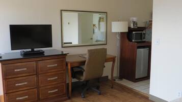 A hotel room with a wooden desk, a television, a mirror, a lamp, a microwave, and a bed.