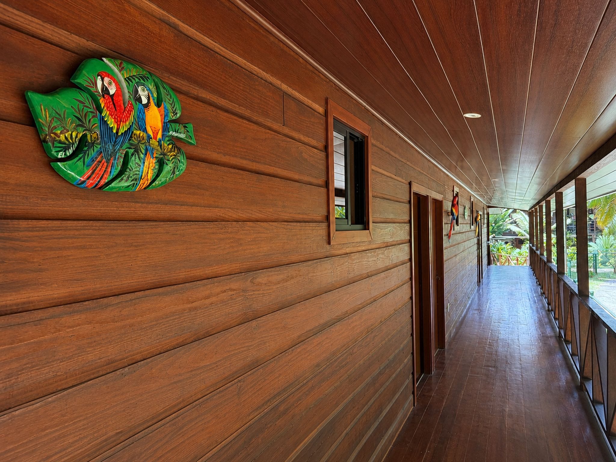 A wooden corridor with a mural of colorful parrots on the left wall.