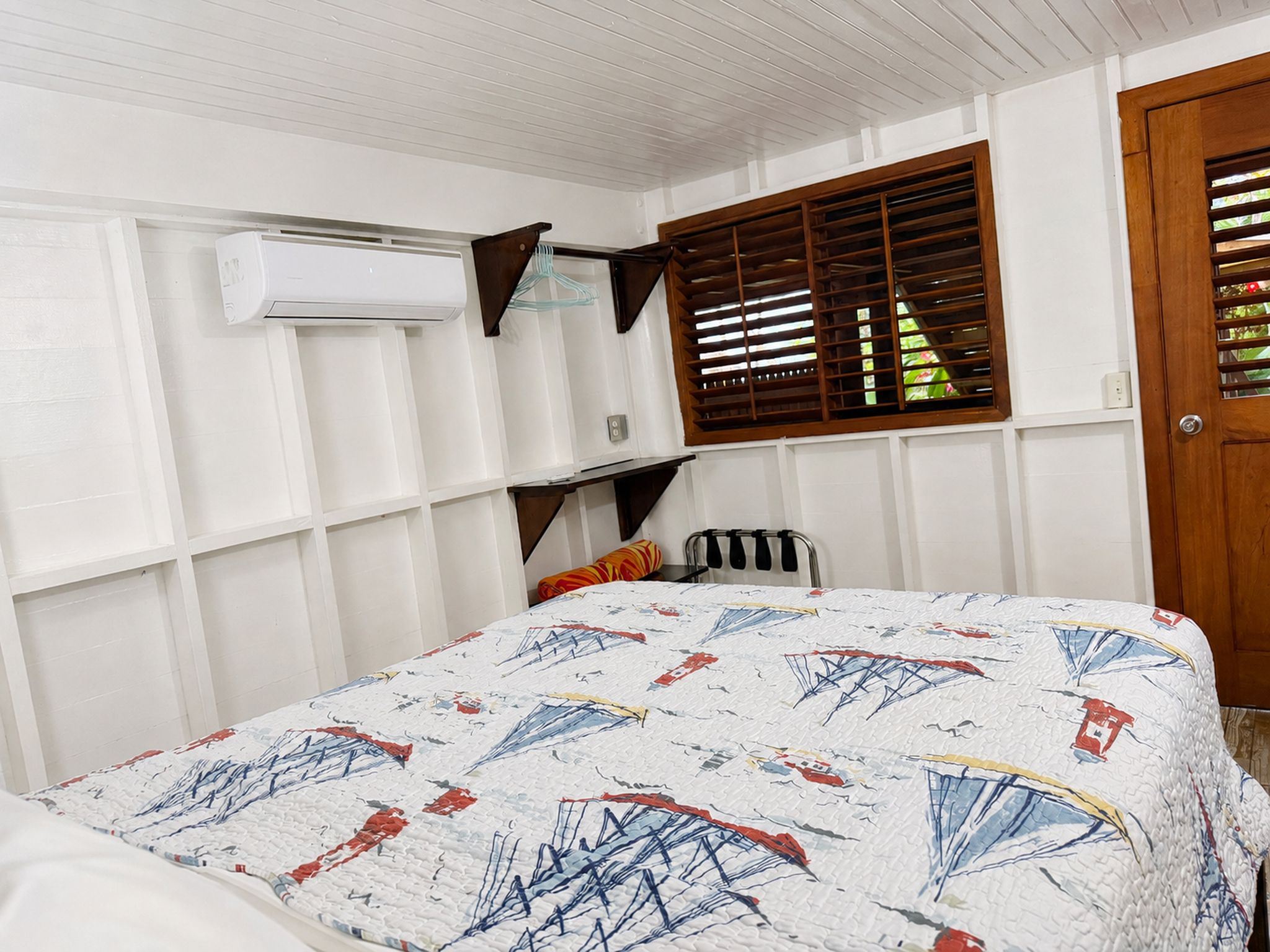 A bedroom with a bed, a window with blinds, an air conditioning unit, and a door.