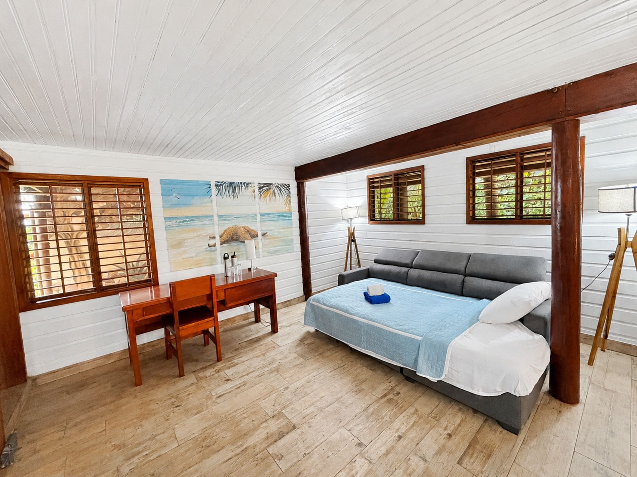 Une chambre à coucher avec un lit, un bureau et une chaise. Il y a des fenêtres avec des volets en bois.