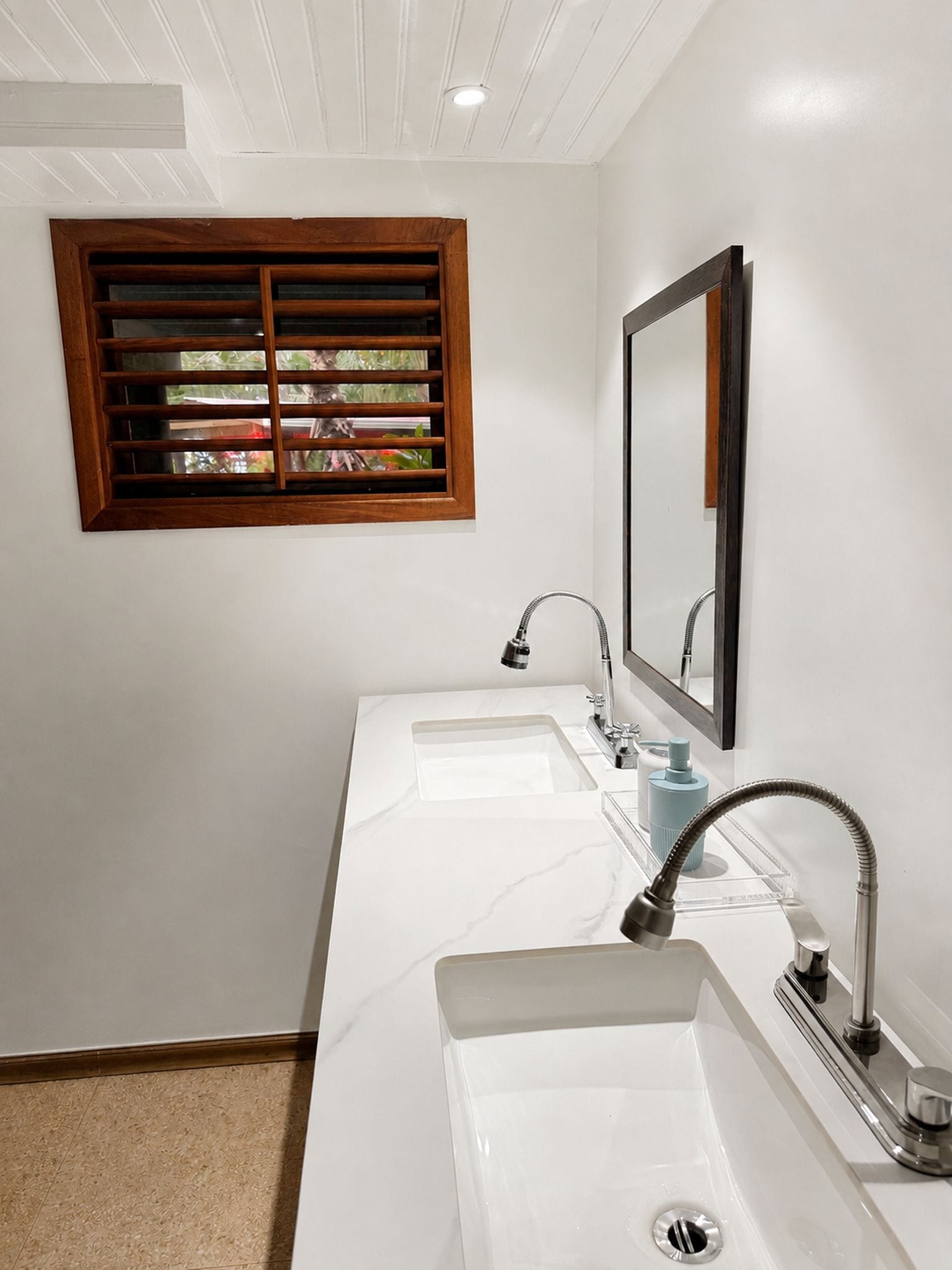 Un baño con dos lavamanos, una ventana con persianas y un espejo.