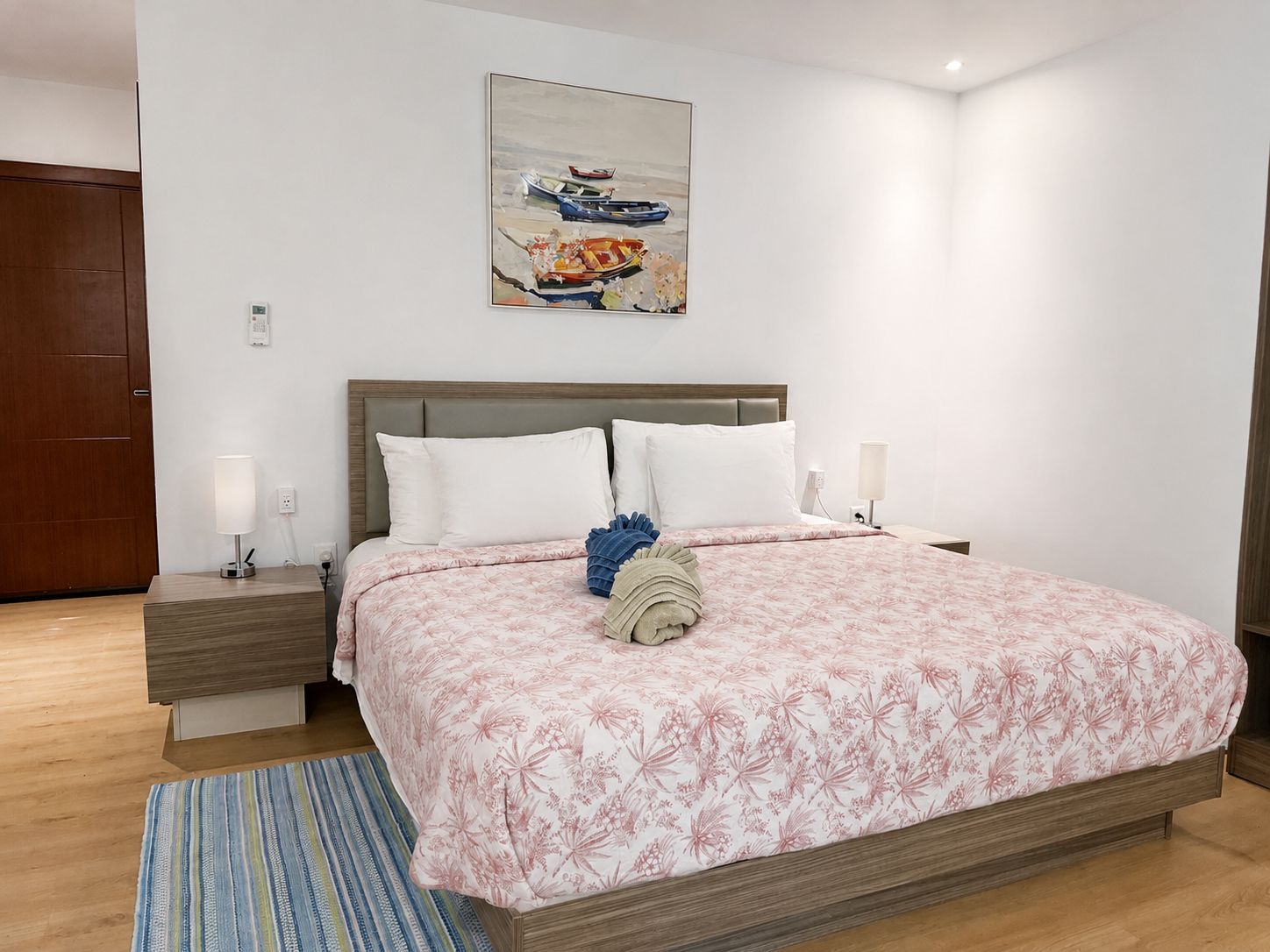A bedroom with a bed, bedside tables, a nightstand, a lamp, a painting, and a wooden door.
