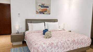 A bedroom with a bed, bedside tables, a nightstand, a lamp, a painting, and a wooden door.