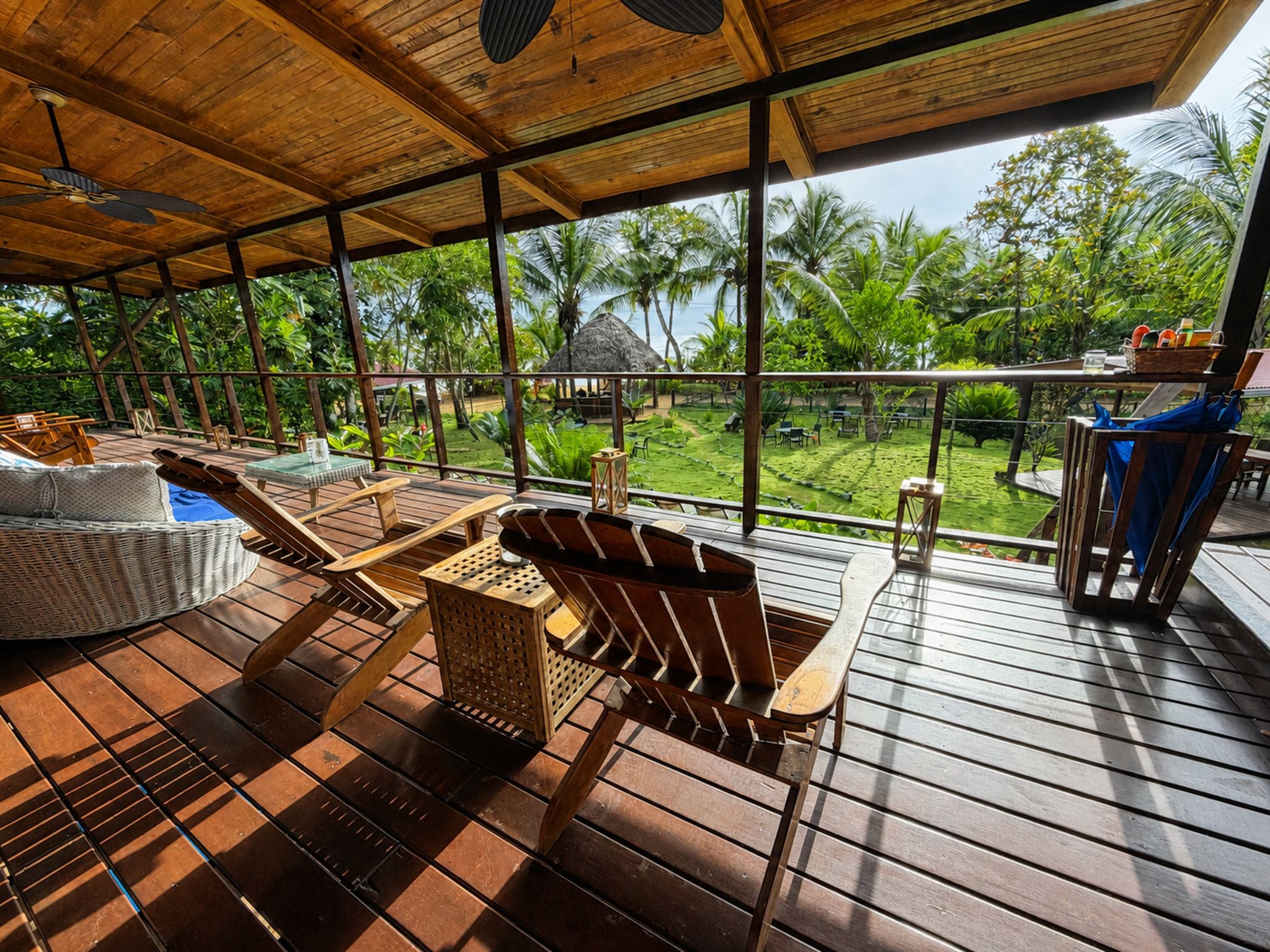 A wooden deck with lounge chairs and a small table, overlooking a lush garden with palm trees.