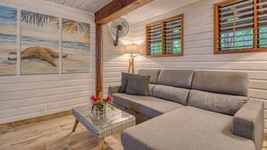 A cozy living room with a grey sofa, a glass coffee table with a vase of flowers, wooden beams on the ceiling, and artwork on the walls. - Oasis Bluff Beach (Bocas del Toro)