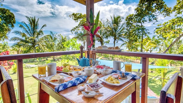 A breakfast table with various dishes and drinks, overlooking a pool and lush greenery. - Oasis Bluff Beach (Bocas del Toro)