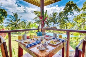 Une table de petit-déjeuner dressée avec divers plats et boissons, donnant sur une piscine et une végétation luxuriante.