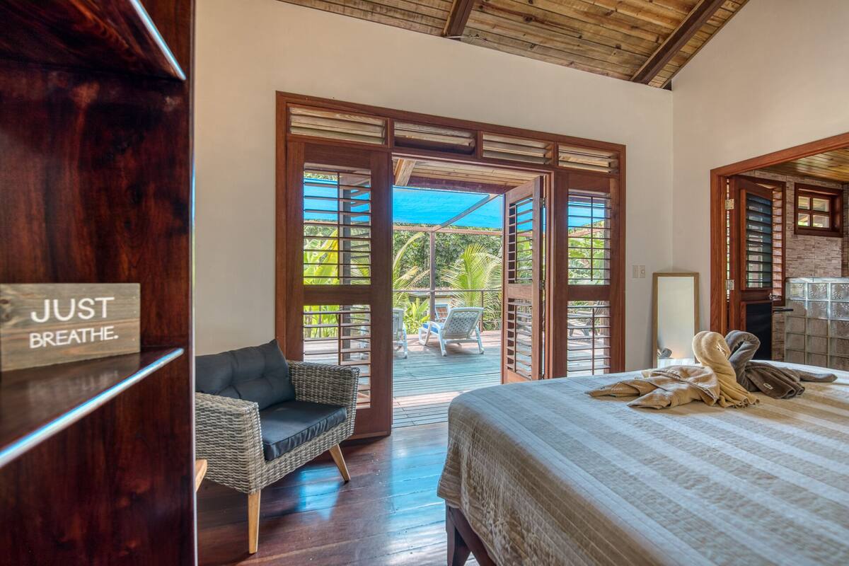 A bedroom with a bed, a chair, and a view of an outdoor area with chairs and a table.
