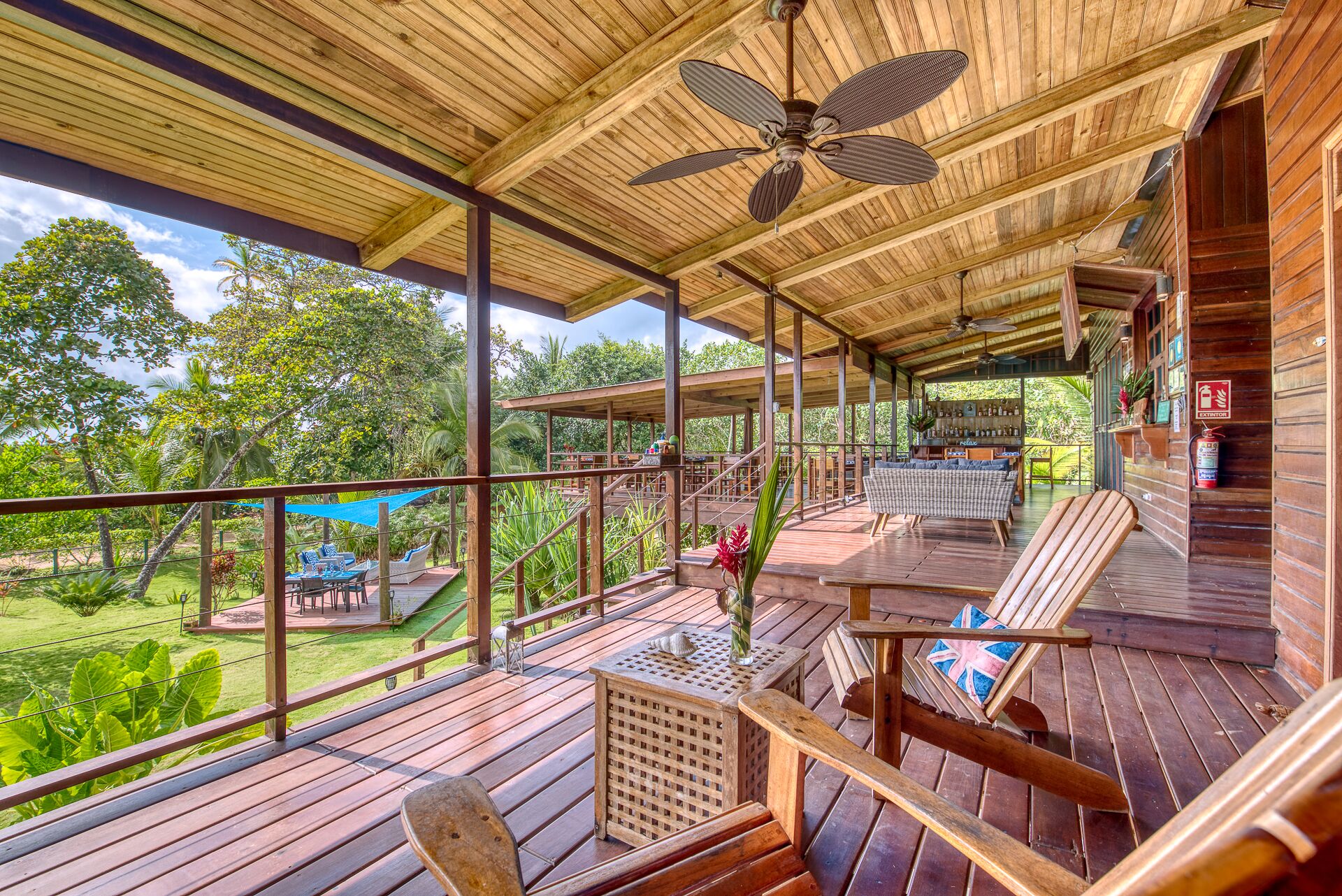 A wooden deck with outdoor seating, a ceiling fan, and a view of the surrounding greenery.