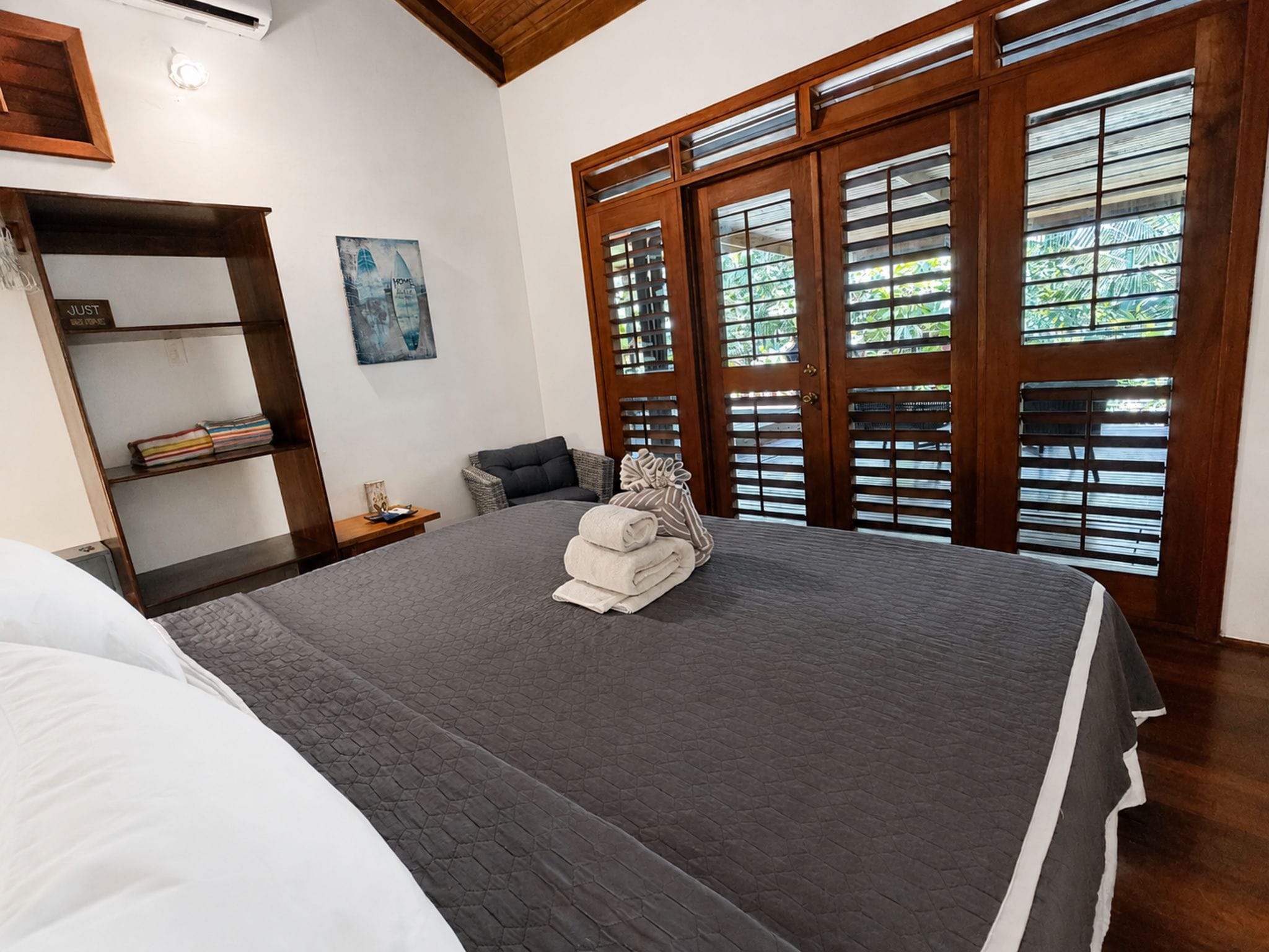 A bedroom with a large bed, a wooden wardrobe, a nightstand, and a window with wooden shutters.