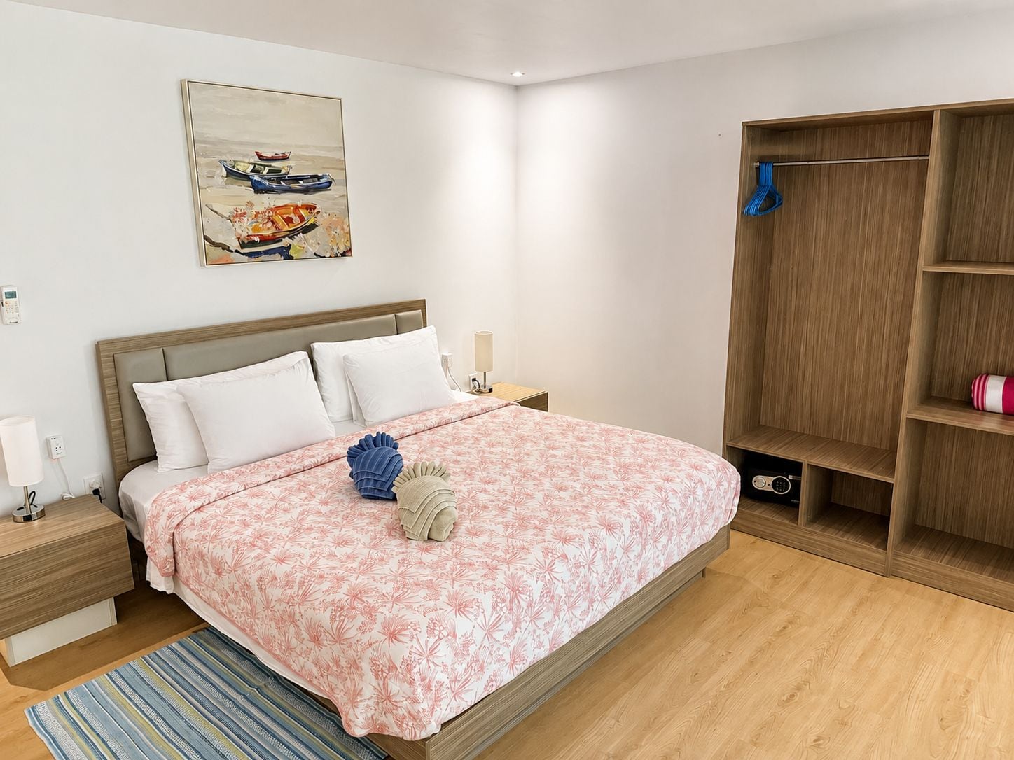 A bedroom with a bed, bedside tables, a nightstand, a wooden wardrobe, a painting, and a striped rug.