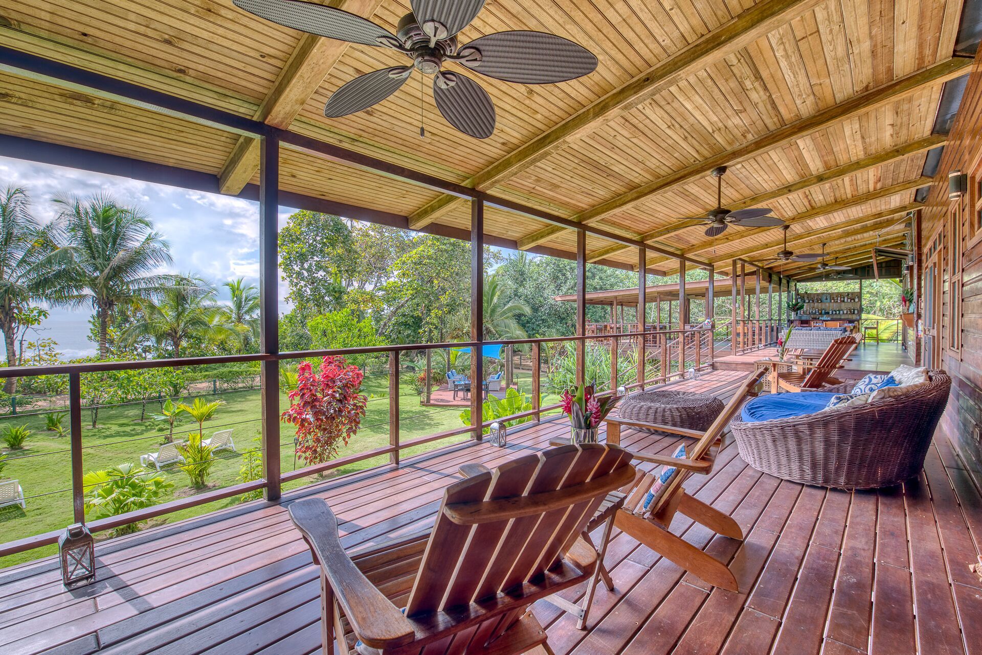 A covered outdoor area with wooden flooring, wicker furniture, and ceiling fans.