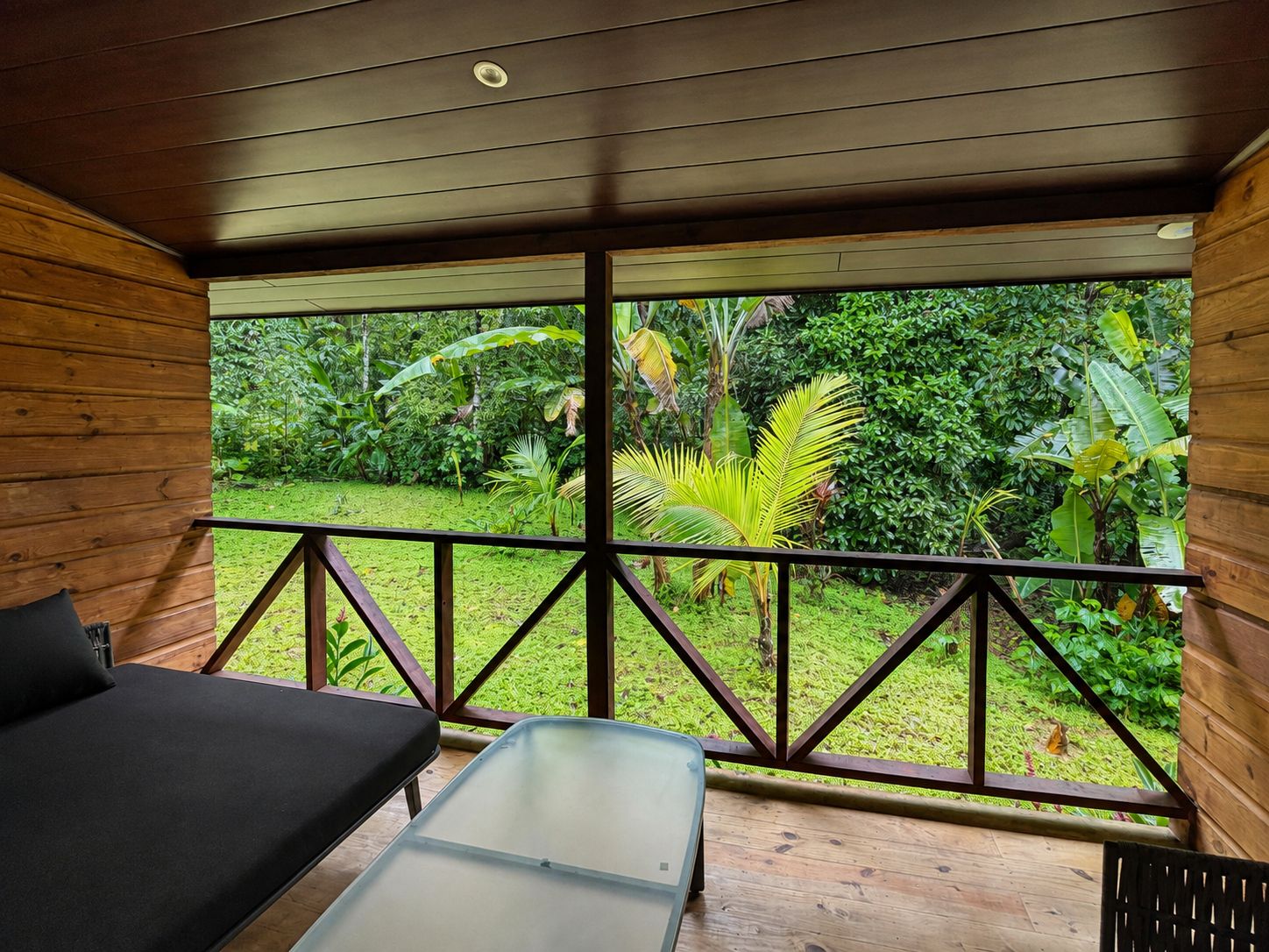 Una habitación de madera con una mesa de vidrio y un banco, con vistas a un jardín exuberante.