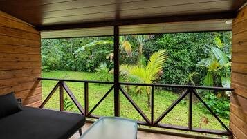 Una habitación de madera con una mesa de vidrio y un banco, con vistas a un jardín exuberante.