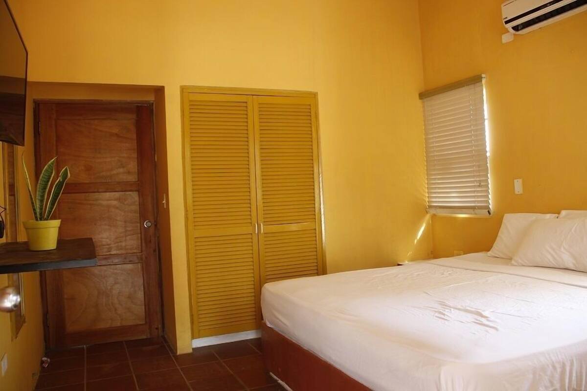 Ein Schlafzimmer mit einem Bett, einer Holztür und einem Fenster mit Jalousien.