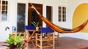 A hammock strung between two windows, a wooden table with blue chairs, and a yellow wall.