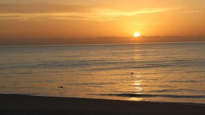 A sunset over a calm sea with a beach in the foreground.