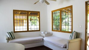 A small, single-room with two beds, a round table, and large windows with wooden frames.