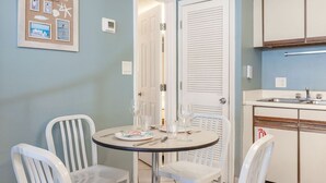 A dining area with a round table and four white chairs, a kitchen with a sink and cabinets, and a door leading to another room. - The Cove 217a 1 Bedroom Condo by RedAwning (Gulf Shores)