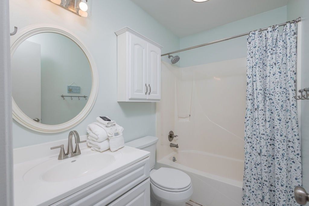 A bathroom with a white sink, mirror, and cabinet, a toilet, and a shower with a patterned curtain.