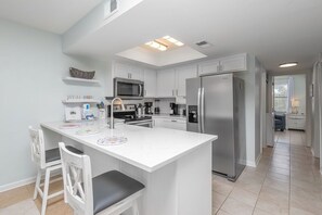 Una cocina moderna con armarios blancos, electrodomésticos de acero inoxidable y una isla central con asientos.