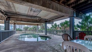An outdoor pool area with concrete flooring, a glass table, and plastic chairs.