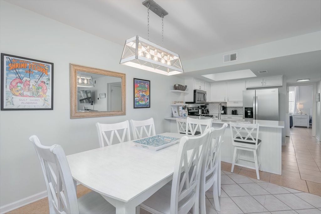 A modern kitchen with white cabinetry, a central island, and a dining area with white chairs and a table.