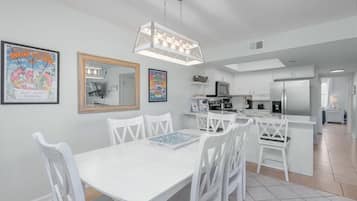 Una cocina moderna con armarios blancos, una isla central y un comedor con sillas y una mesa blancos.