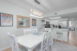A modern kitchen with white cabinetry, a central island, and a dining area with white chairs and a table.