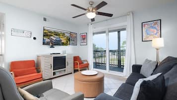A living room with a ceiling fan, a television, a sofa, a coffee table, and a view of the outdoors through a sliding glass door.
