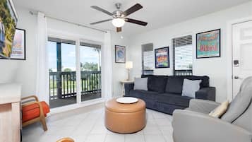 A living room with a ceiling fan, a sofa, a coffee table, and a view through a sliding glass door to a balcony.