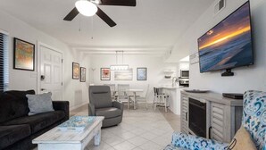 A modern living room with a sofa, armchair, and coffee table. There is a TV mounted on the wall and a ceiling fan.