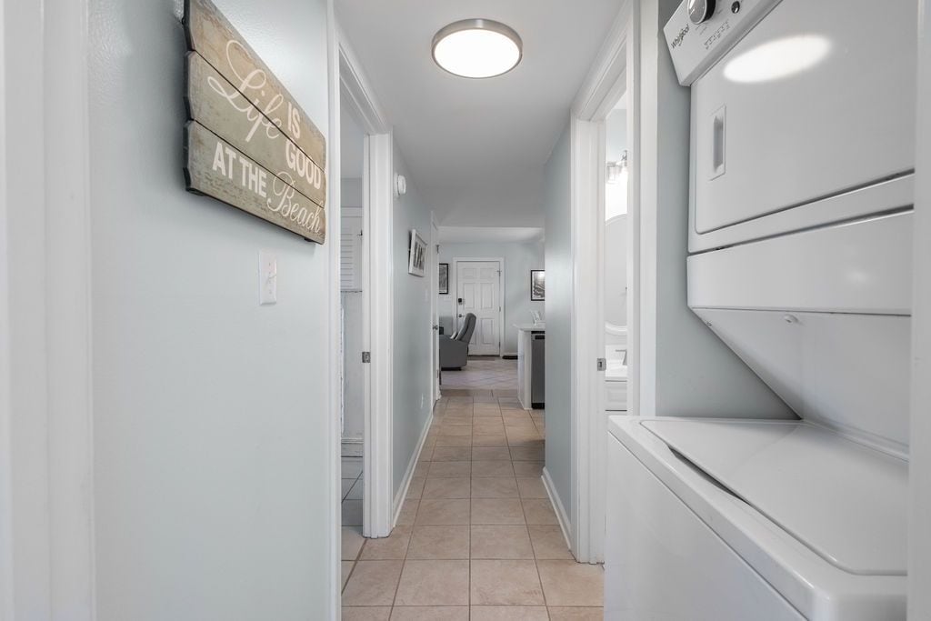 A laundry room with a white washing machine and dryer, a wooden sign with text, and a tiled floor.