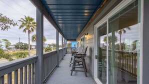 A covered porch with a railing, a seating area with chairs, and a view of the street and palm trees.