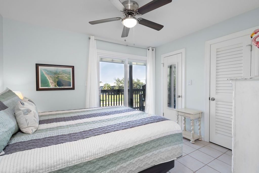 A bedroom with a bed, a ceiling fan, a window, and a door.