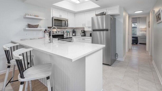 A modern kitchen with white cabinetry, a central island, stainless steel appliances, and a skylight.