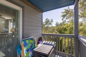 A covered balcony with a wooden bench and a colorful chair, overlooking a wooded area. - Sandy Shores West 101 2 Bedroom Condo by RedAwning (Gulf Shores)