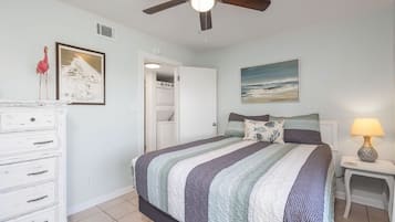 A bedroom with a bed, a dresser, a ceiling fan, a painting, and a lamp.
