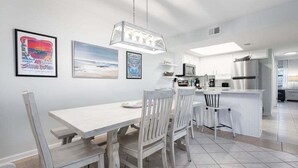 A modern kitchen with white cabinetry, a central island, and a dining area with a wooden table and chairs.