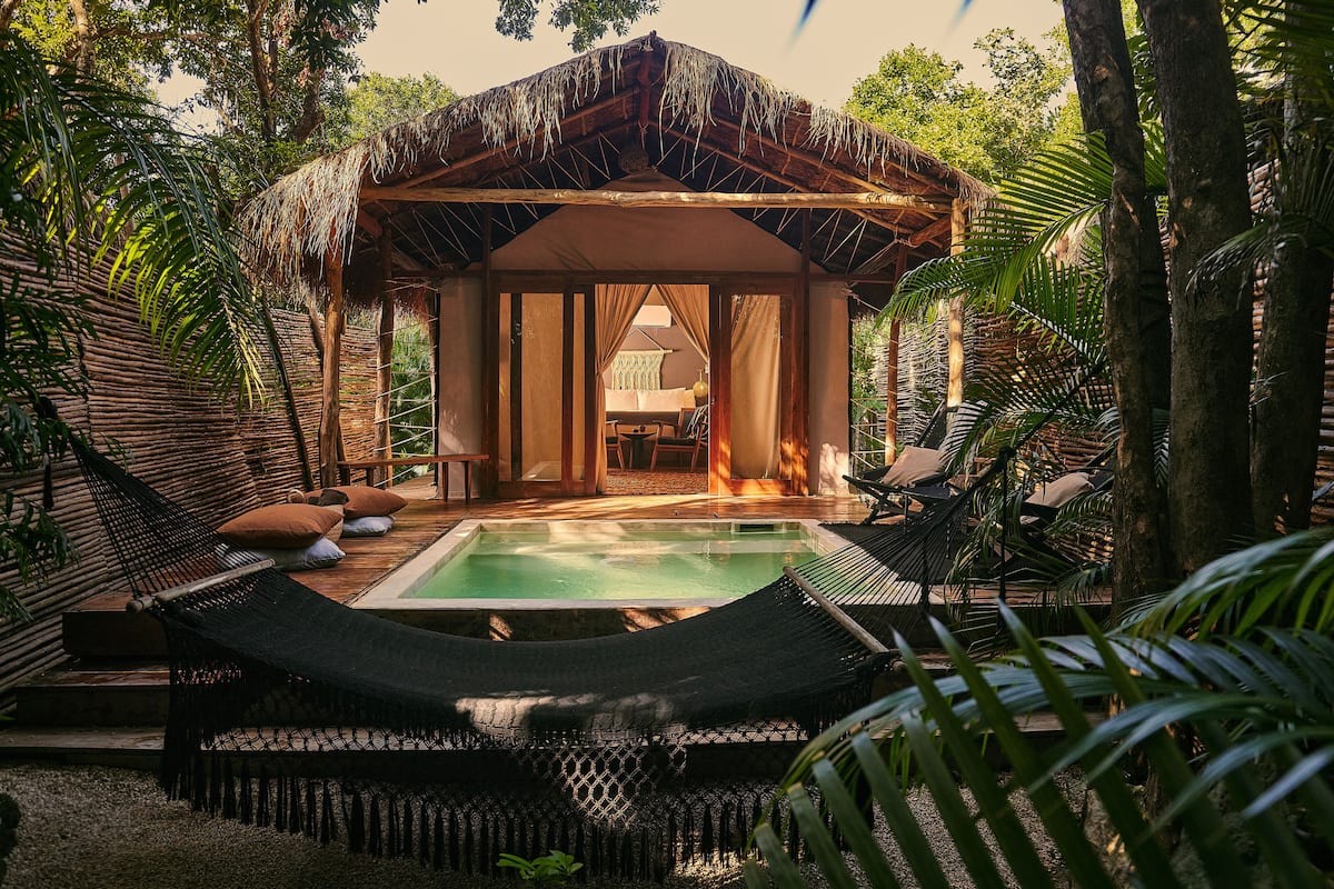 Una estructura con techo de paja, piscina y hamacas.