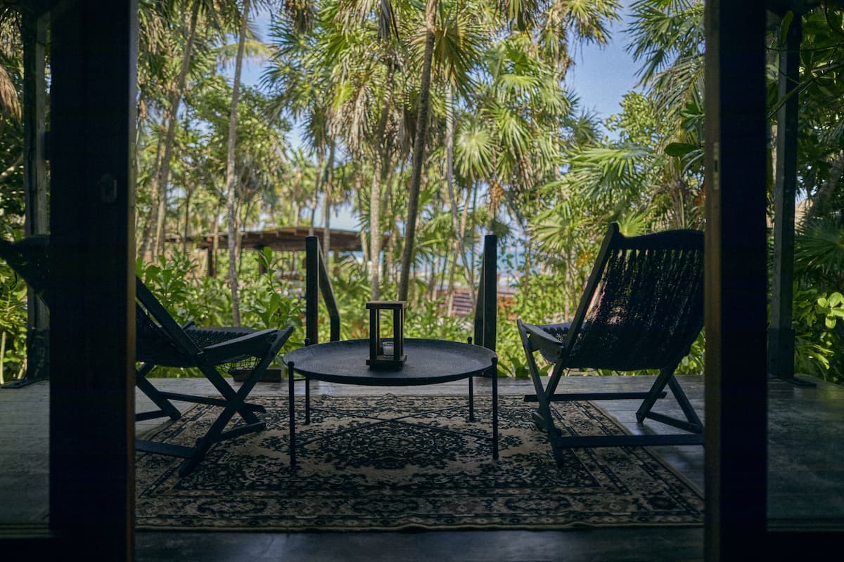 Una habitación con vista a palmeras, dos sillas, una mesa y un farol.